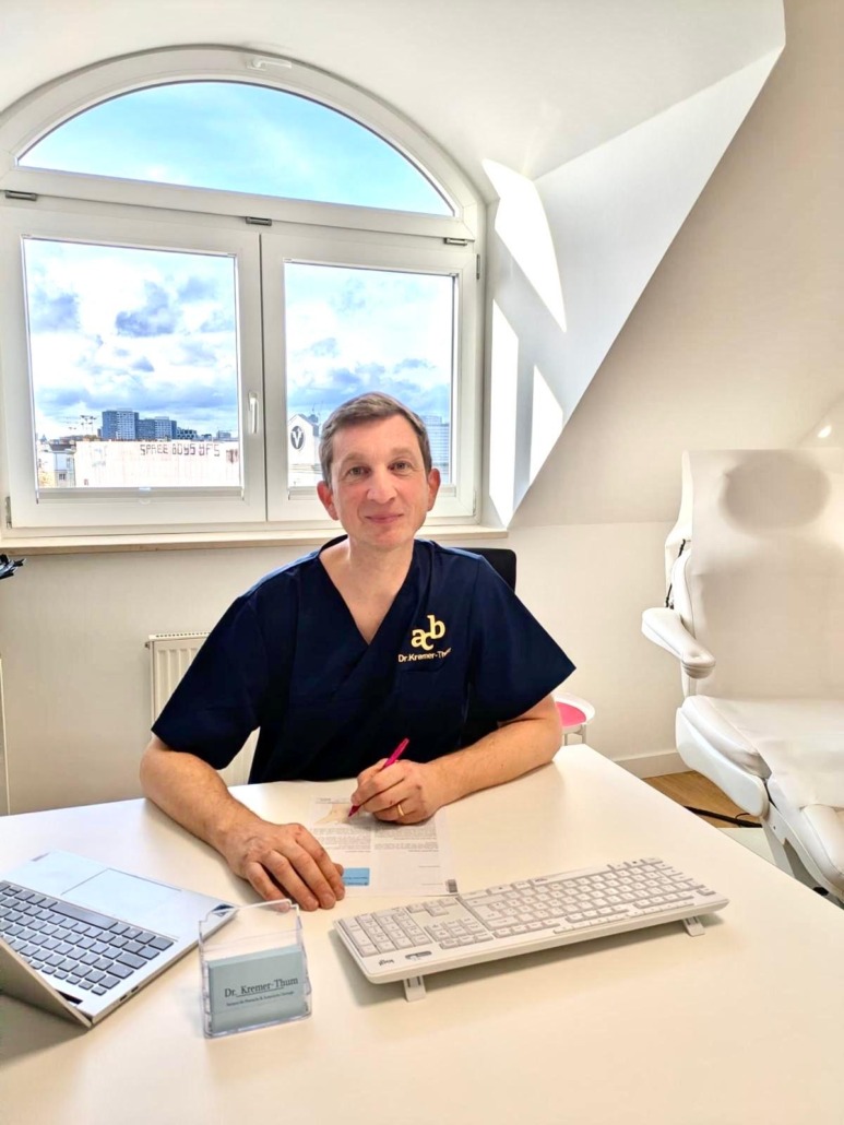 ausfuehrliche-beratung-in-der-schoenheitschirurgie-in-berlin-von-dr-kremer-thum Dr. med. Kremer-Thum sitzt an seinem Schreibtisch in seiner Berliner Schönheitschirurgie.