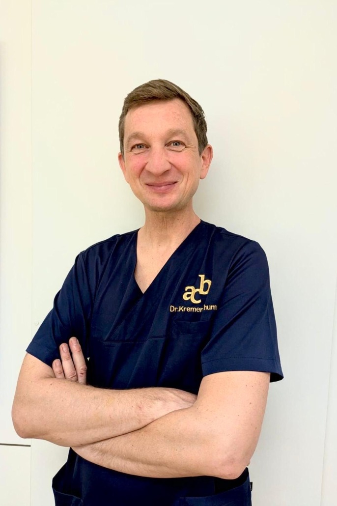 dr-kremer-thum-schoenheitschirurg-berlin Foto, das Dr. Kremer-Thum lächelnd in seiner Praxis zeigt.
